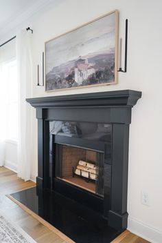 a fireplace with a painting above it in a living room next to a rug and window