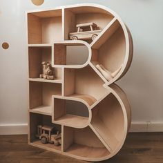 a wooden shelf with cars and toys in it on the floor next to a wall