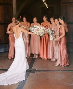 a group of women standing next to each other in front of a wooden door holding bouquets