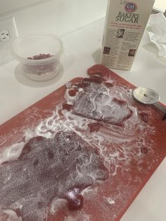 a red cutting board sitting on top of a counter next to a bowl and spoon