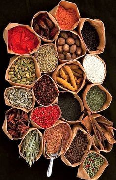 an array of spices and herbs arranged in small bowls on a black surface with spoons