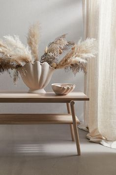 a table with two vases on it and some dried plants in front of the window