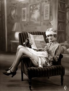 an old photo of a woman sitting in a chair reading a newspaper with her legs crossed