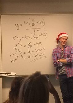 a man standing in front of a whiteboard wearing a santa hat