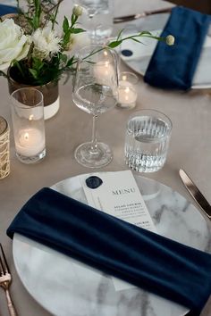 the table is set with white and blue linens, silverware, candles, and flowers