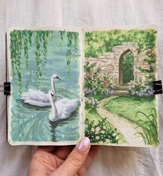 a hand holding an open book with watercolors on it and a drawing of a swan