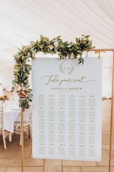 an elegant seating sign with greenery and gold calligraphy is displayed in front of a white tent