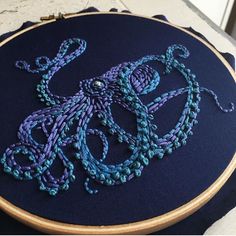 an embroidered octopus on a blue and purple background is displayed in front of a wooden frame