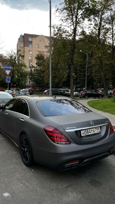 a car parked in a parking lot next to some trees and grass with buildings in the background