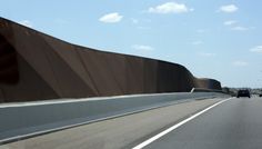 cars driving on the highway next to a large wall that looks like a curved road