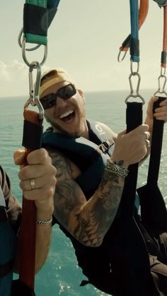 a man with tattoos on his arm holding onto two ropes in the air while smiling at the camera