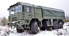 an army truck parked in the middle of a snowy field with trees and bushes behind it