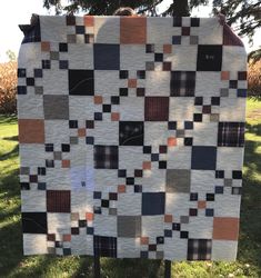 a patchwork quilt hanging from a clothes line in the grass with trees in the background