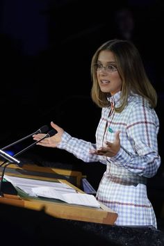 a woman standing at a podium with her hands in the air while giving a speech