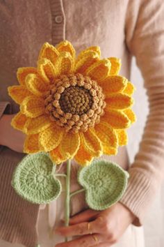 a woman holding a crocheted sunflower in her hands