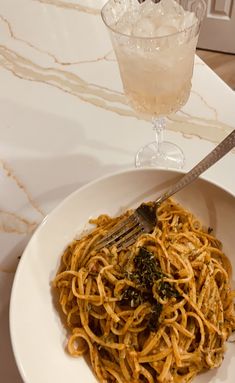 a white bowl filled with pasta and spinach next to a glass of ice water