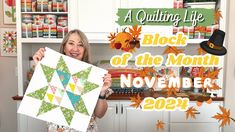 a woman holding up a quilt in front of a kitchen counter with autumn decorations on it