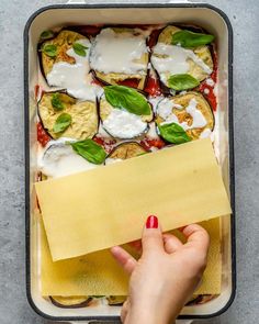 a person holding a piece of paper over a casserole dish with cheese and spinach