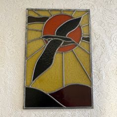 a stained glass window with a bird on it's side and the sun in the background