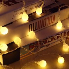 some books are stacked on top of each other with white lights strung from the ends