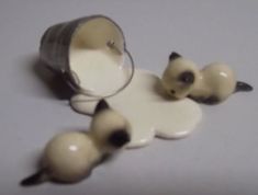 two small ceramic cats sitting on top of a white table next to a canister