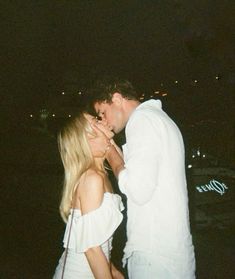 a man kissing a woman on the cheek in front of a boat at night time