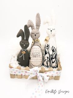 three stuffed bunnies sitting in a basket on top of a white surface with a ribbon