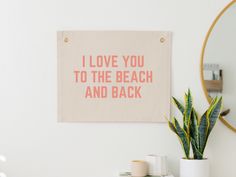 a pink and white wall hanging next to a potted plant on top of a table