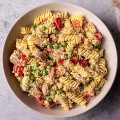 a white bowl filled with pasta salad on top of a gray table next to a fork