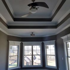 an empty room with three windows and a ceiling fan in the middle of the room