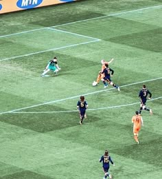 a group of soccer players running on the field during a game with one player blocking the ball