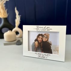 a white photo frame sitting on top of a table next to a vase with flowers