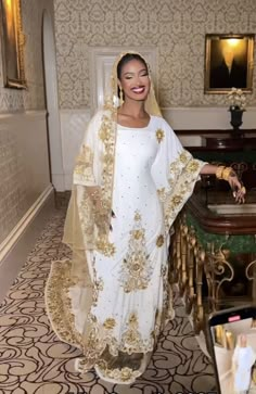 a woman in a white and gold outfit standing next to a table with flowers on it