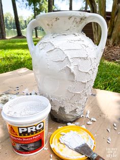 a large white vase sitting on top of a wooden table next to a yellow plate