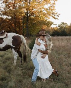 a man and woman are hugging in the grass next to a brown and white horse