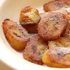 a white bowl filled with fried bananas covered in powdered sugar