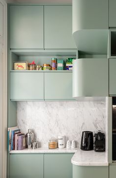 a kitchen with green cabinets and marble counter tops, along with coffee maker in the corner