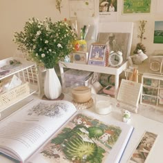 an open book sitting on top of a white table next to pictures and flowers in vases