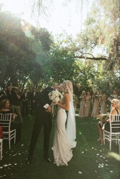 a bride and groom standing in front of an outdoor ceremony with white flowers on the grass