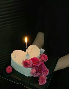 a heart shaped cake with flowers and a single candle on the top that is lit