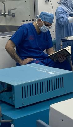 two doctors in scrubs and masks are looking at an electronic device