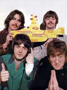 the beatles posing for a photo in front of a yellow submarine shaped object with two thumbs up