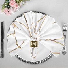 a table setting with white and gold plates, silverware and napkins on it