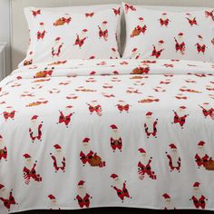 a bed with white sheets and red christmas decorations on it, along with two pillows