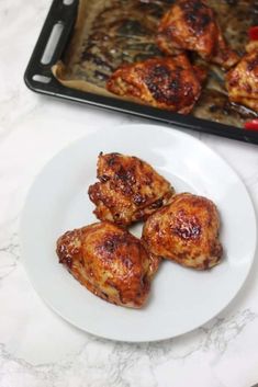 four pieces of chicken on a white plate next to a baking sheet and spatula