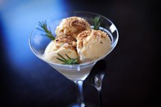 three scoops of ice cream in a martini glass with rosemary sprigs on top