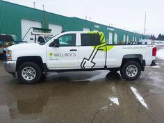 a white truck parked in front of a building with green and yellow lettering on it