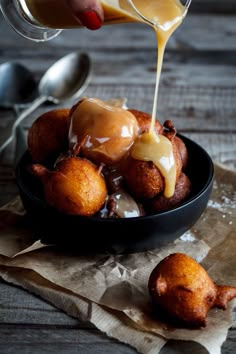 some food is being drizzled with sauce in a black bowl on a wooden table