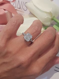 a woman's hand with a diamond ring on it and a flower in the background