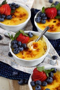 three bowls filled with pudding and berries on top of a blue cloth next to two spoons